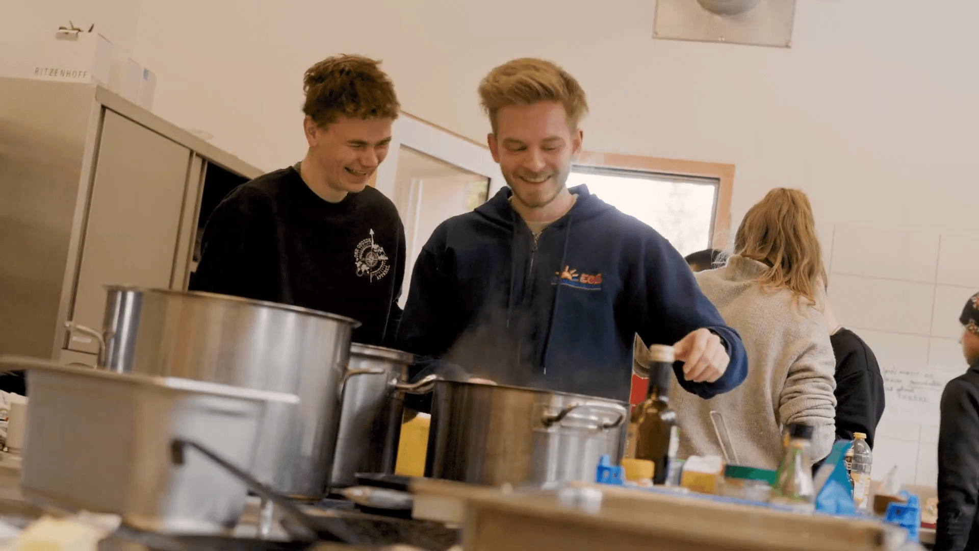 Zwei junge Teamer kochen lachend in der Küche des Gruppenhauses