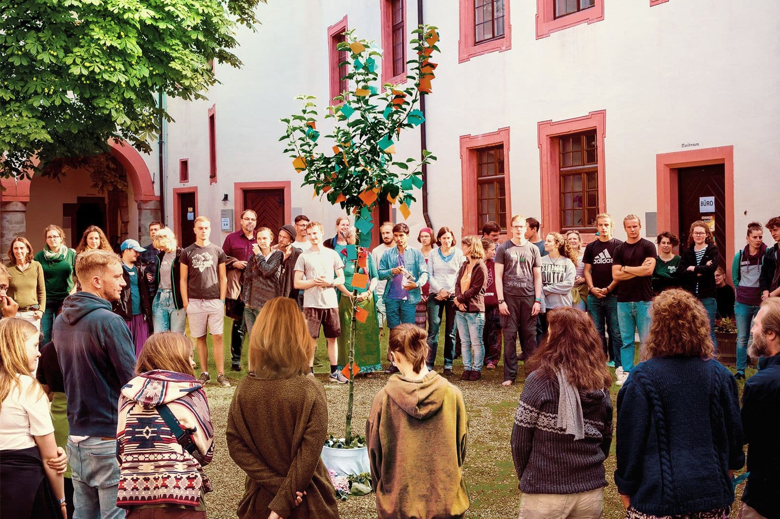 Große Gruppe steht im Kreis im Innenhof eines Gruppenhauses