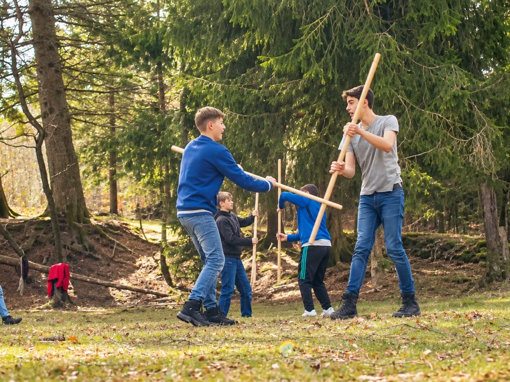 Jugendliche arbeiten auf einer sonnigen Waldlichtung gemeinsam mit Holzstäben